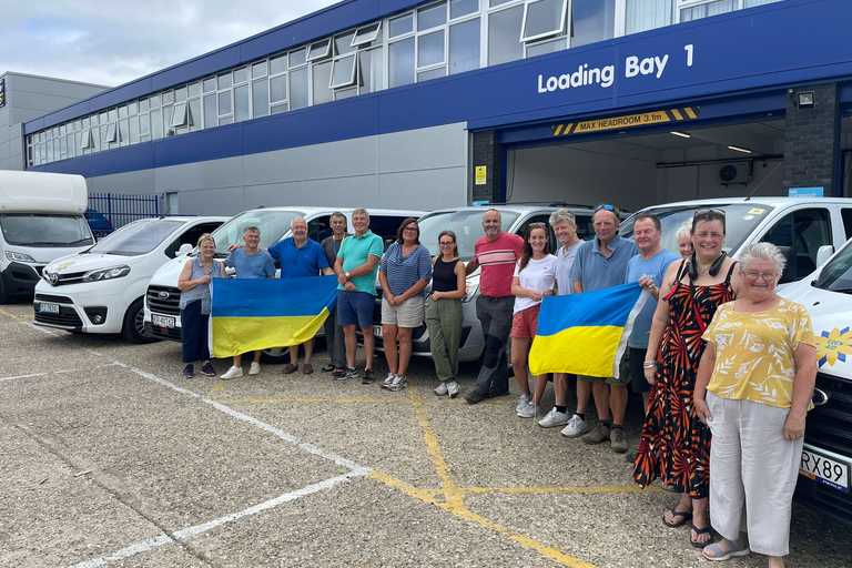 A team of volunteers posing next to a loading bay holding up Ukrainian flags