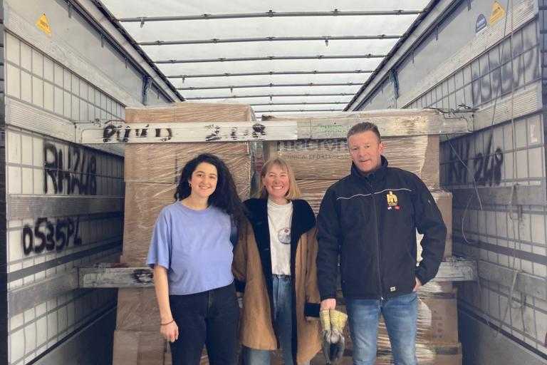 Two volunteers and a truck driver posing for a photo inside a truck they have filled with boxes of donated items