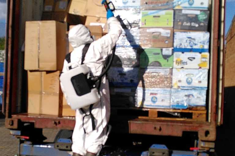 A person in PPE gear, fumigating a truck full of boxes