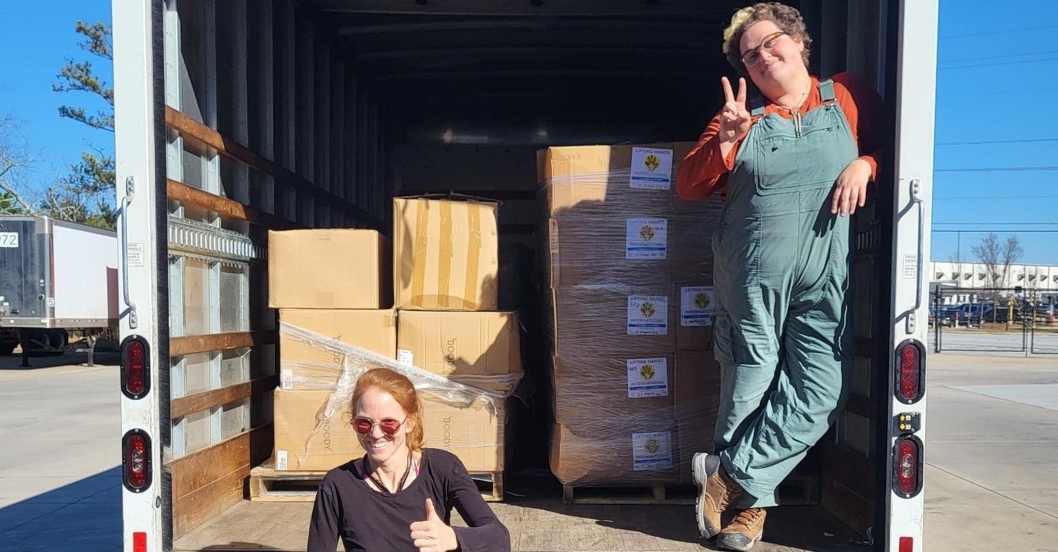 Two team members of the Gulf Disaster Network posing happily at the back of a truck that is already half filled with boxes full of aid supplies.