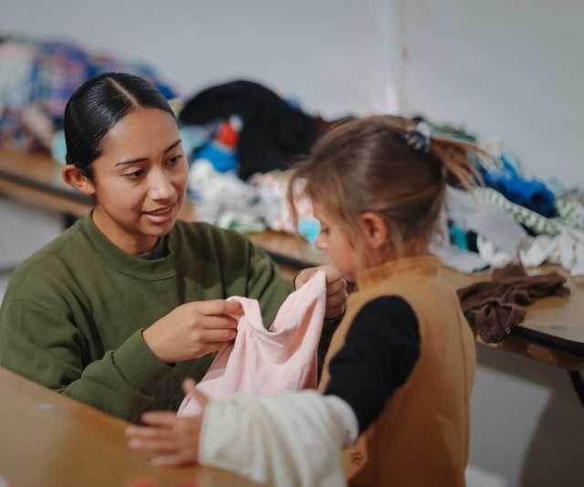 A volunteer holding up some clothes to a little girl to check for size