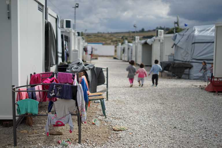 A refugee camp, with three young children with the backs turned walking in the distance