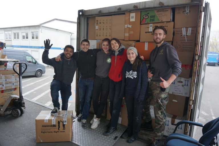 Volunteers standing next to a truck they have filled to full capacity with boxes of donated items, posing for a photo