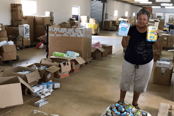 A volunteer holding up donated food items for babies – that have been delivered, in a warehouse