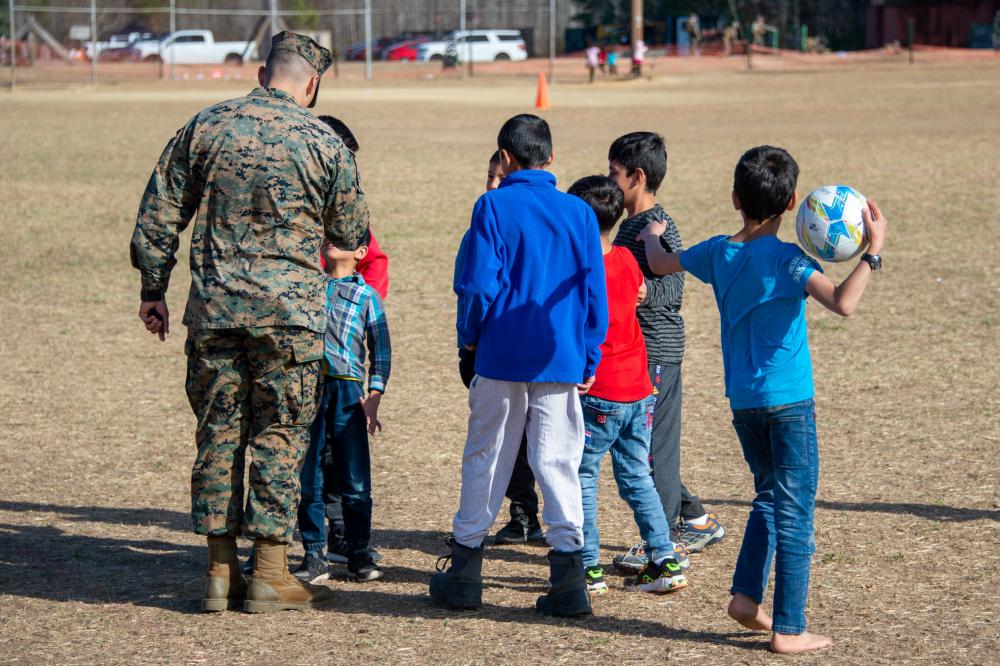 A US Marine in camouflage uniform playing football with Afghan boys.
